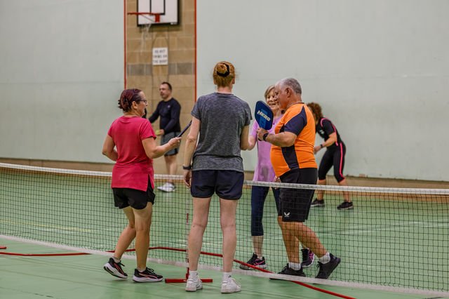 A small group of pickleball players gathered with paddles on an indoor court
