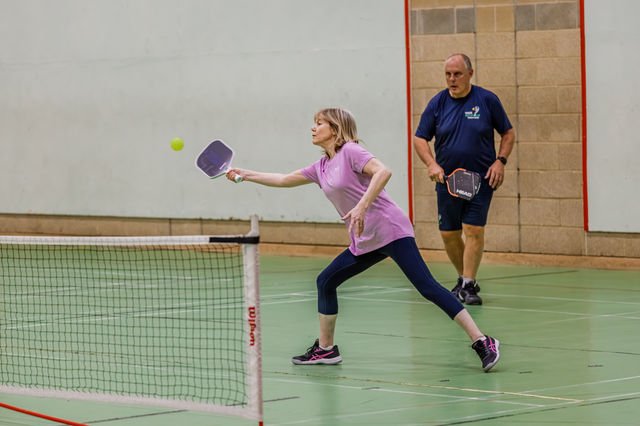 A pickleball player reaching to return the ball near the net