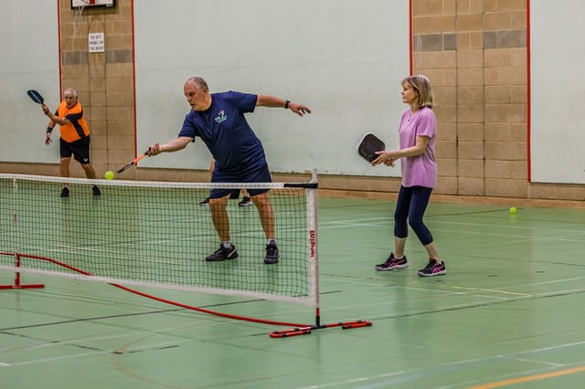 A pickleball player stretching forward to play a volley at the net